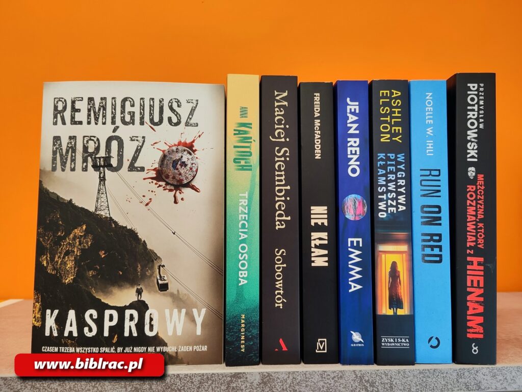 Na zdjęciu osiem książek ustawionych na półce - pierwsza po lewej stoi zwrócona okładką w stronę aparatu, jest to książka pt. Kasrpwy autorstwa Remigiusza Mroza. Dalej stoją książki, których widać jedynie grzbiety, a na nich tytuły i autorzy książek, którzy są wymienieni w artykule.