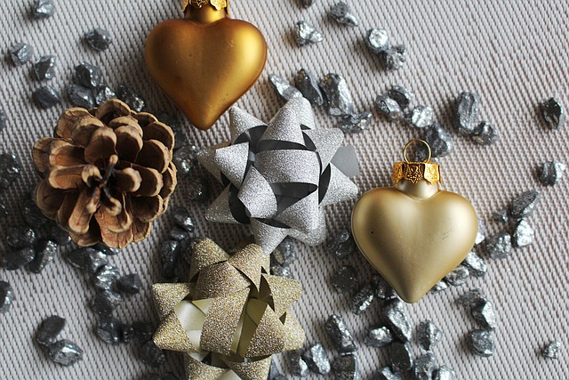 Na zdjęciu / grafice widać rozłożone na prążkowanym obrusie / tle ozdoby świąteczne - gwiazdki zrobione ze wstążek lub pasków papieru (brokatowych), szyszkę, 2 bombki złote w kształcie serduszek