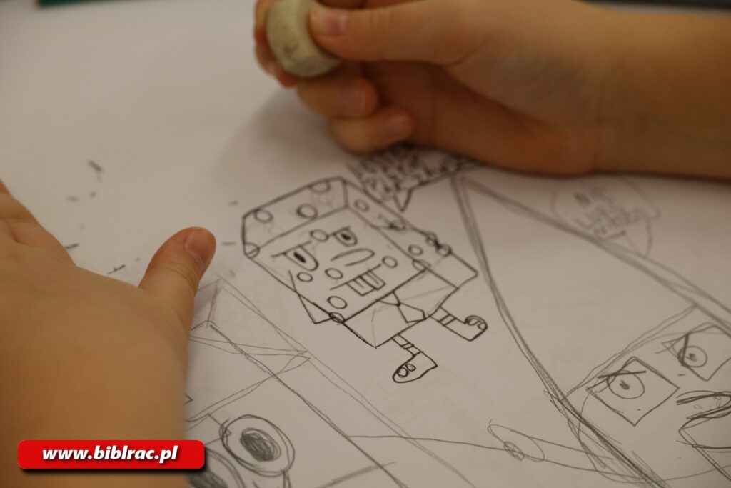 Na zdjęciu zbliżenie na dziecięce dłonie oparte o leżący na stole szkic przedstawiający Sponge Boba (postać z kreskówki), jedna dłoń trzyma gumkę do gumowania