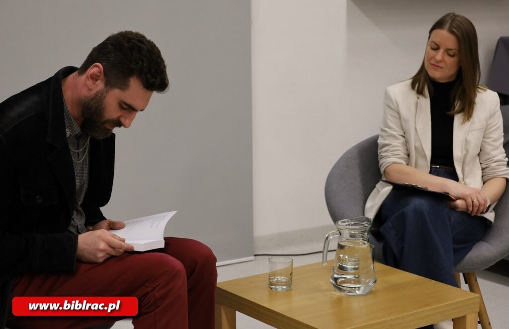 Na zdjęciu z lewej strony siedzący przy małym kwadratowym drewnopodobnym stoliczka mężczyzna w ciemnoczerwonych spodniach i czarnej marynarce (noszący brodę, włosy ciemne), pochylający się i czytający książkę, którą trzyma na kolanach. Z prawej strony zdjęcia, po drugiej stronie stoliczka, kobieta (raczej młoda) siedząca na szarym fotelu - dżinsy z szerokimi nogawkami, jasna marynarka, włosy za ramiona, oczy przymknięte. Na stoliczku szklanki i dzbanek z wodą.