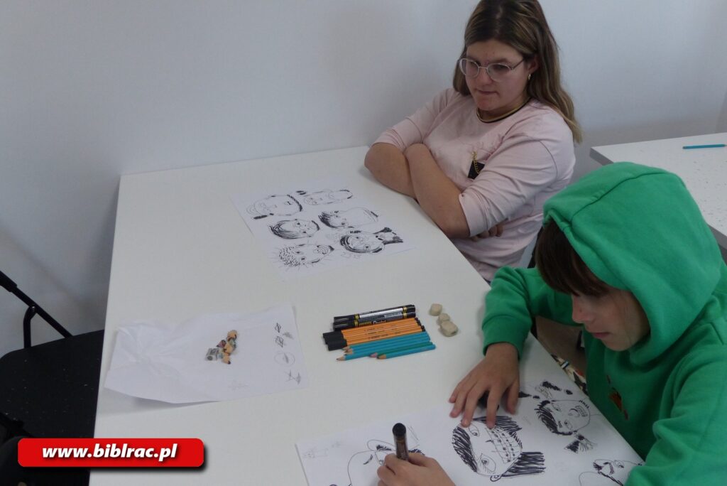 Na zdjęciu dwoje dzieci przy białym stole rysujących postacie czarnym flamastrem - chłopak ok 11-12 lat w zielonej bluzie z założonym kapturem oraz dziewczyna ok 13 -15 lat w okularach (akurat w danym momencie nie rysuje - siedzi z założonymi rękami i patrzy jak rysuje chłopak w zielonej bluzie).