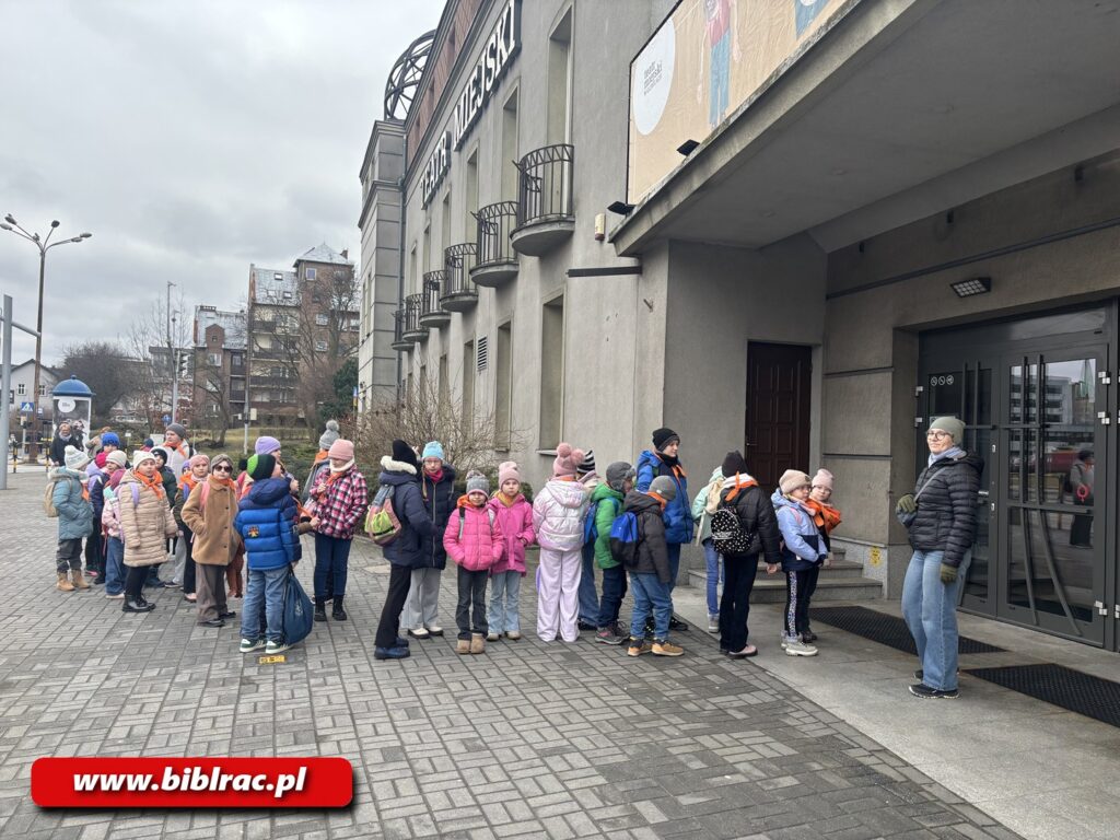 Na zdjęciu dzieci stojące przed budynkiem w kolejce do wejścia.