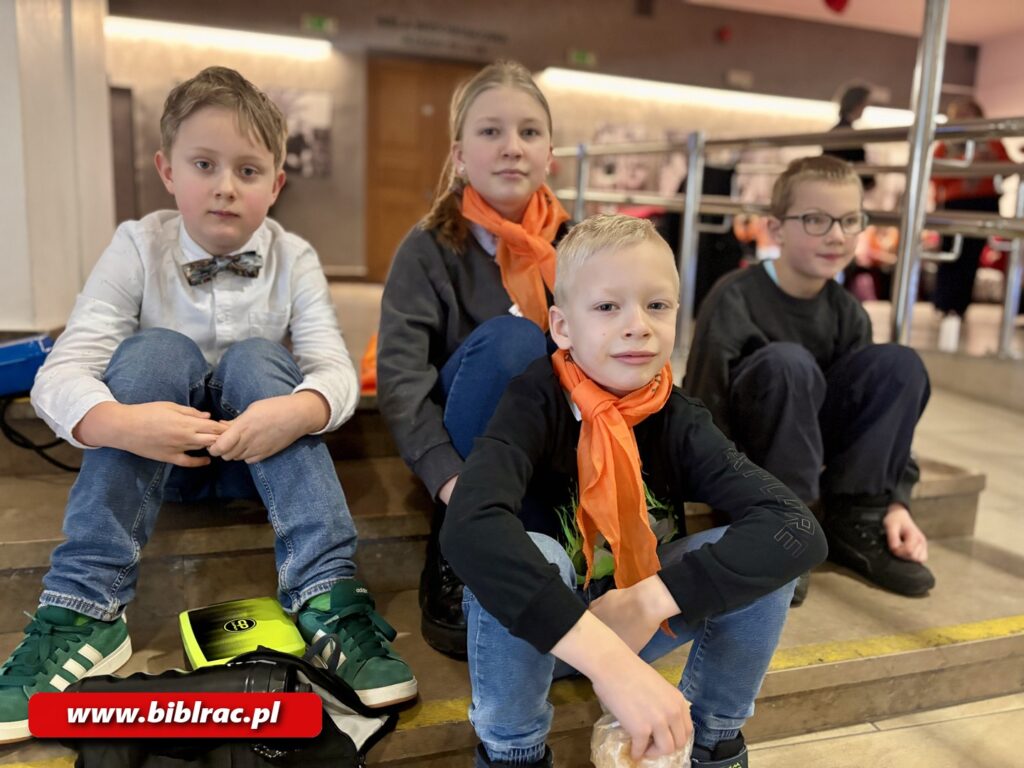 Na zdjęciu 4 dzieci siedzących na schodach w holu.