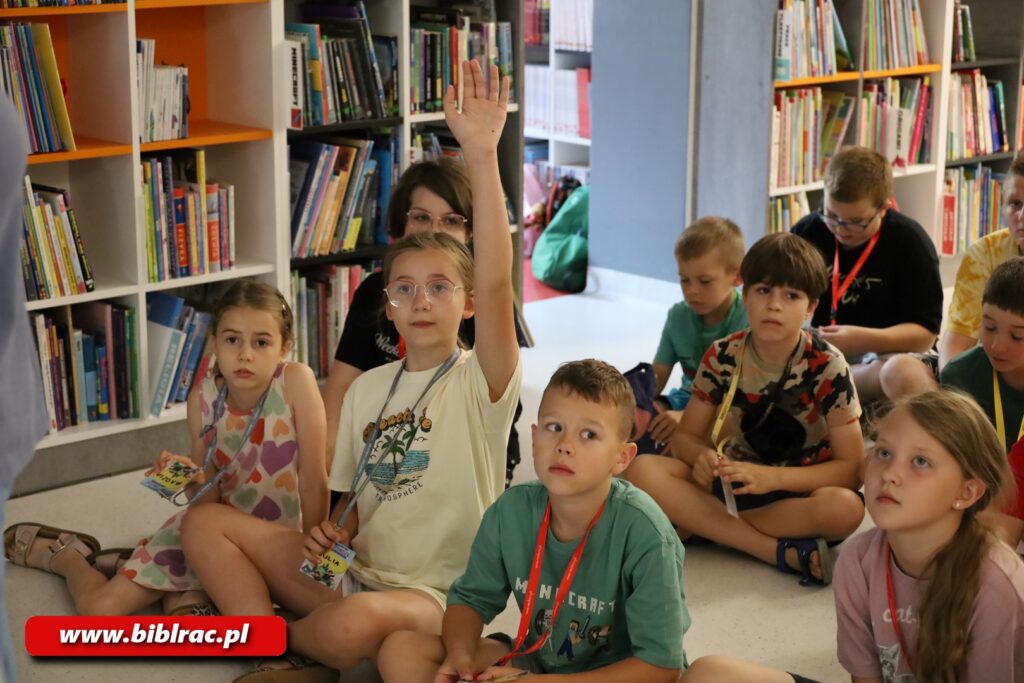 Na zdjęciu dzieci siedzące na podłodze w pomieszczeniu biblioteki