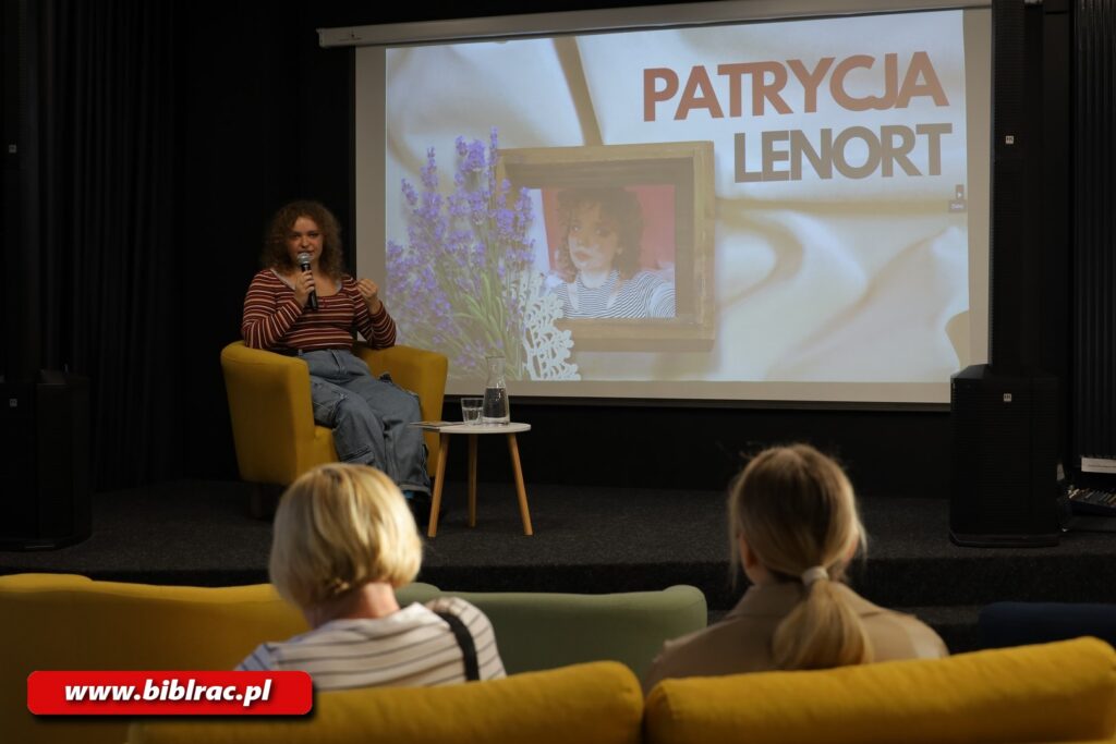 Na zdjęciu kobieta na scenie siedząca w żółtym fotelu. N ekranie za kobietą wyświetlona grafika oraz napis Patrycja Lenort.